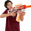 A young person wearing safety glasses and a maroon t-shirt is holding and aiming a red and white X-Shot Hyper Gel Trace Fire toy gun. Voir les images du produit