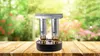A paraffin heater sits on a wooden table with a blurred garden background. Produktbild-Vorschau