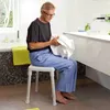 An elderly man sits on a white shower stool in a modern bathroom, holding a white towel. Produktbild-Vorschau