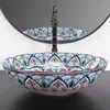 A decorative ceramic sink with a colorful pattern is shown in a bathroom setting, with a faucet and mirror in the background. Náhled obrázku produktu