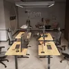 An office setting with multiple height-adjustable desks and chairs. Produktbild-Vorschau