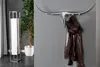 A bull head coat rack mounted on a gray wall, with a brown leather jacket hanging on it. A tall floor lamp and a potted plant are visible on the left. Produktbild-Vorschau