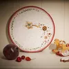 A Christmas-themed plate with cookies and decorations, next to a pomegranate and a wooden rocking horse. Náhled obrázku produktu