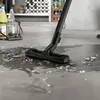 A vacuum cleaner nozzle is cleaning up broken glass and liquid on a concrete floor. Produktbild-Vorschau