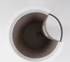 Top-down view of a planter with a white outer rim and a brown inner pot. A section of the inner pot is peeled back, revealing a black serrated edge. Voir les images du produit