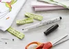 A flat lay of sewing and crafting supplies, including fabric labels, a marker, scissors, and pins, arranged on a wooden surface. Produktbild-Vorschau