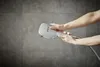 A person's hands holding a chrome shower head against a tiled wall. Anteprima dell’immagine prodotto