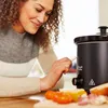 A woman is using a chalkboard marker to write on a Russell Hobbs slow cooker. There are some food items on the table in front of her. Podgląd zdjęcia produktu