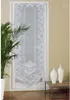 A white lace door curtain hanging on a door frame, with a potted plant to the left and decorative vases on a table to the right. Produktbild-Vorschau