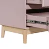 A close-up view of the lower section of a pink dresser with wooden legs and an open drawer showing metal drawer slides. Náhled obrázku produktu