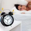 A woman is covering her ears with a pillow as an alarm clock rings. Voir les images du produit