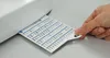 A hand is holding a card with stitch patterns from a sewing machine. Produktbild-Vorschau