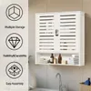 A white bathroom cabinet with slatted doors is mounted on a tiled wall above a sink with a faucet. Podgląd zdjęcia produktu