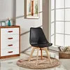 A black chair with wooden legs sits on a rug in a room with a dresser and a framed picture on the wall. Náhled obrázku produktu