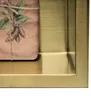A close-up view of a product wrapped in brown paper with a botanical illustration, placed within a gold frame. Produktbild-Vorschau