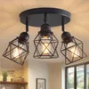 A black ceiling lamp with three adjustable spotlights, each with a cage-like shade, is mounted on a ceiling. Produktbild-Vorschau