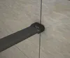 A close-up view of a black shower door handle attached to a glass panel, with a light-colored tiled wall in the background. Produktbild-Vorschau
