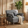 A gray sleeper armchair with a beige throw blanket is placed in a living room setting with beige curtains and a potted plant. Produktbild-Vorschau