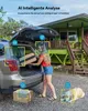 A woman is loading luggage into the trunk of a car in front of a house, with a dog lying on the ground nearby. The scene is set outdoors. Produktbild-Vorschau