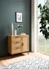 A modern sideboard with rattan details is placed in a room with a dark teal wall and a large window. A rug with a geometric pattern is on the floor. Produktbild-Vorschau