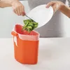 A person is shown discarding food scraps into an orange kitchen bin lined with a white bag. Podgląd zdjęcia produktu