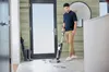 A man is using a vacuum cleaner in a hallway near a door. Voir les images du produit