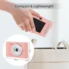 A hand holding a pink digital camera over a bag. Náhled obrázku produktu