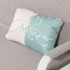 A close-up of a pillow with the word 'Amore' written on it, placed on a gray sofa. Produktbild-Vorschau