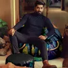A man is sitting on a beanbag chair with a colorful elephant print. There is a small stool in front of him and plants in the background. Voir les images du produit