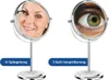Two vanity mirrors are shown side-by-side on a white background. The left mirror shows a woman applying mascara, labeled '1:1 Spiegelung'. The right mirror shows a close-up of an eye, labeled '7-fach Vergrößerung'. Produktbild-Vorschau