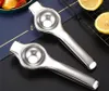Two silver manual citrus juicers are placed on a dark surface, with some lemons and fruit pieces in the background. Produktbild-Vorschau