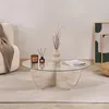 A round glass coffee table with a travertine base, decorated with a vase, a candle, and a magazine, placed on a rug in a living room setting. Anteprima dell’immagine prodotto