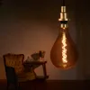 A vintage-style light bulb hangs in the foreground, with a chair and table in the background. Anteprima dell’immagine prodotto