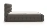 A side view of a dark gray upholstered bed frame with a white mattress on a white background. Produktbild-Vorschau