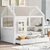 A white wooden house-shaped bed with drawers, set in a room with artwork on the wall and a desk in the background. Voir les images du produit