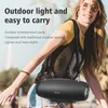 A woman is carrying a black speaker over her shoulder outdoors. Produktbild-Vorschau
