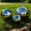 Three polished stainless steel garden spheres of different sizes are placed on a grassy lawn next to a piece of driftwood. Podgląd zdjęcia produktu