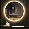 A modern bathroom with a bathtub, shelves, and decorative items reflected in a circular LED mirror. Voir les images du produit