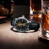 A watch is placed on a table next to a glass of whiskey and a candle. Produktbild-Vorschau