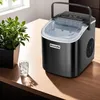 An ice maker sits on a wooden table next to a glass of ice water and a potted plant. Náhled obrázku produktu