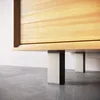 A close-up view of the bottom of a wooden cabinet or furniture piece, showing its legs resting on a concrete floor. Produktbild-Vorschau