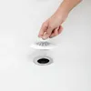 A hand is placing a white drain stopper and hair catcher over a sink drain. Voir les images du produit