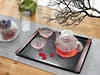A tea set with a teapot, cups, and a decorative jar is arranged on a tray on a table, with a decorative branch overhead. Produktbild-Vorschau