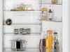 Interior view of an open refrigerator with various food items and containers on shelves. Produktbild-Vorschau