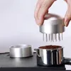 A hand is holding a coffee distributor tool over a portafilter filled with coffee grounds. Náhľad obrázku produktu