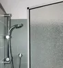 A close-up view of a shower head and a textured glass shower door. Produktbild-Vorschau