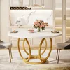 A round white dining table with a gold base, set in a modern dining room with chairs and kitchen cabinets in the background. Podgląd zdjęcia produktu