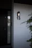 A modern house entrance with a black door and a white brick wall featuring a black outdoor light fixture and the number 15. Anteprima dell’immagine prodotto