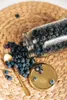 Blueberries spilling out of a glass jar onto a woven mat, with a golden spoon and lid nearby. Produktbild-Vorschau