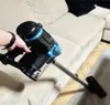 A hand is holding a black and blue vacuum cleaner, using it to clean a beige sofa. Podgląd zdjęcia produktu
